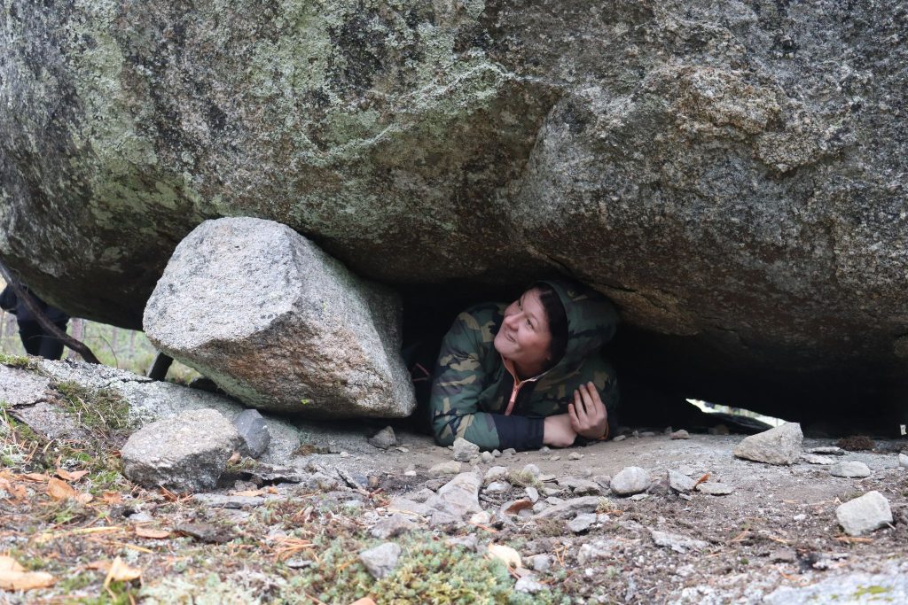 Nainen kurkistaa kiven alta